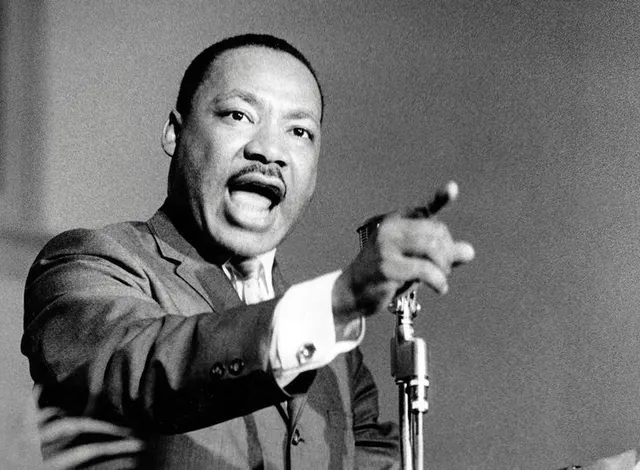 Martin Luther King Jr. hablando ante un micrófono y señalando hacia el público en una fotografía en blanco y negro