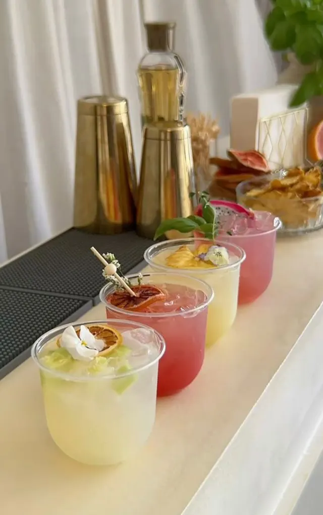 Four colorful drinks with ice and fruit or floral garnishes